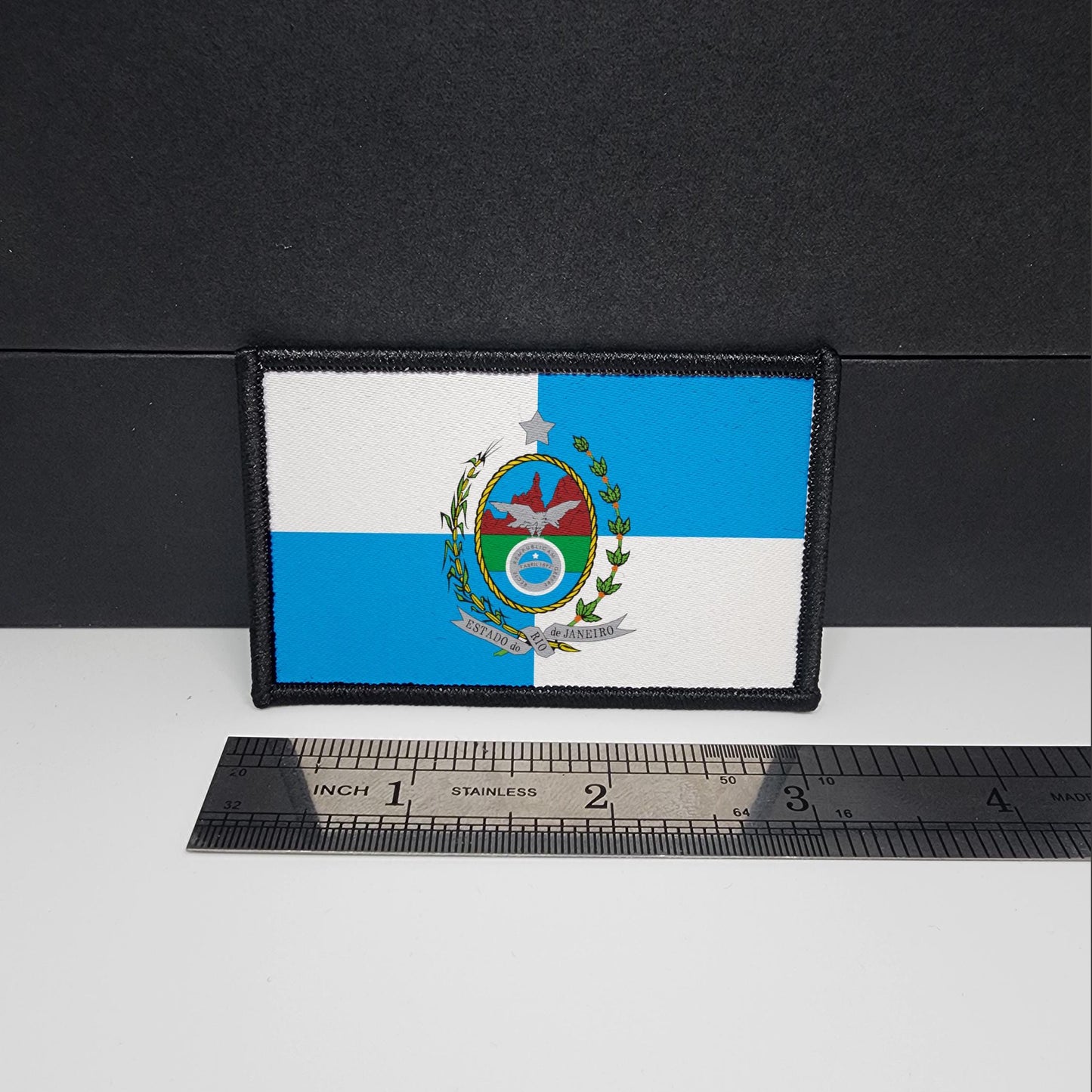 A rectangular patch featuring the Rio de Janeiro flag, displayed against a black background next to a ruler for scale.
CAPS LOCK ORIGINAL - patch - morale patch - 2x3 inch – hook and loop - iron-on - interchangeable patch - hat - bag - camping patch - travel patch