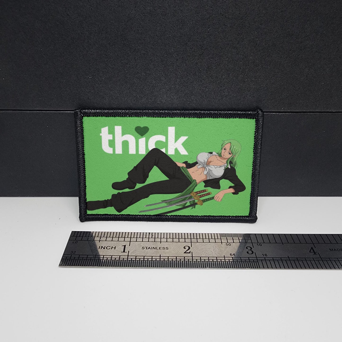 Patch with a graphic design and 'thick' text on a green background, next to a ruler for scale.
Thick Hearts – morale patch – sexy - anime - waifu - video game - 2x3 inch – hook and loop - iron-on – interchangeable patch hat -Zoro - Pirate hunter - Straw hat crew