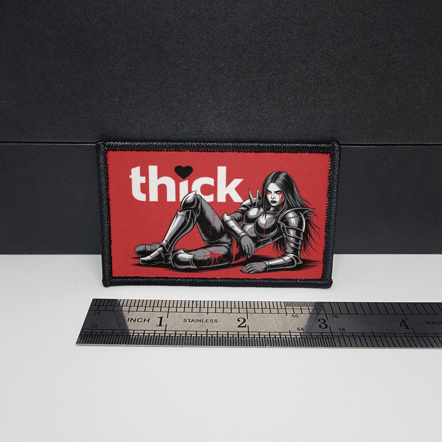 Patch with a graphic of a woman and the word 'thick' on a red background, next to a ruler for scale.
Thick Hearts – morale patch – sexy - anime - waifu - video game - 2x3 inch – hook and loop - iron-on – interchangeable patch hat - Fallen Knight waifu - metal waifu