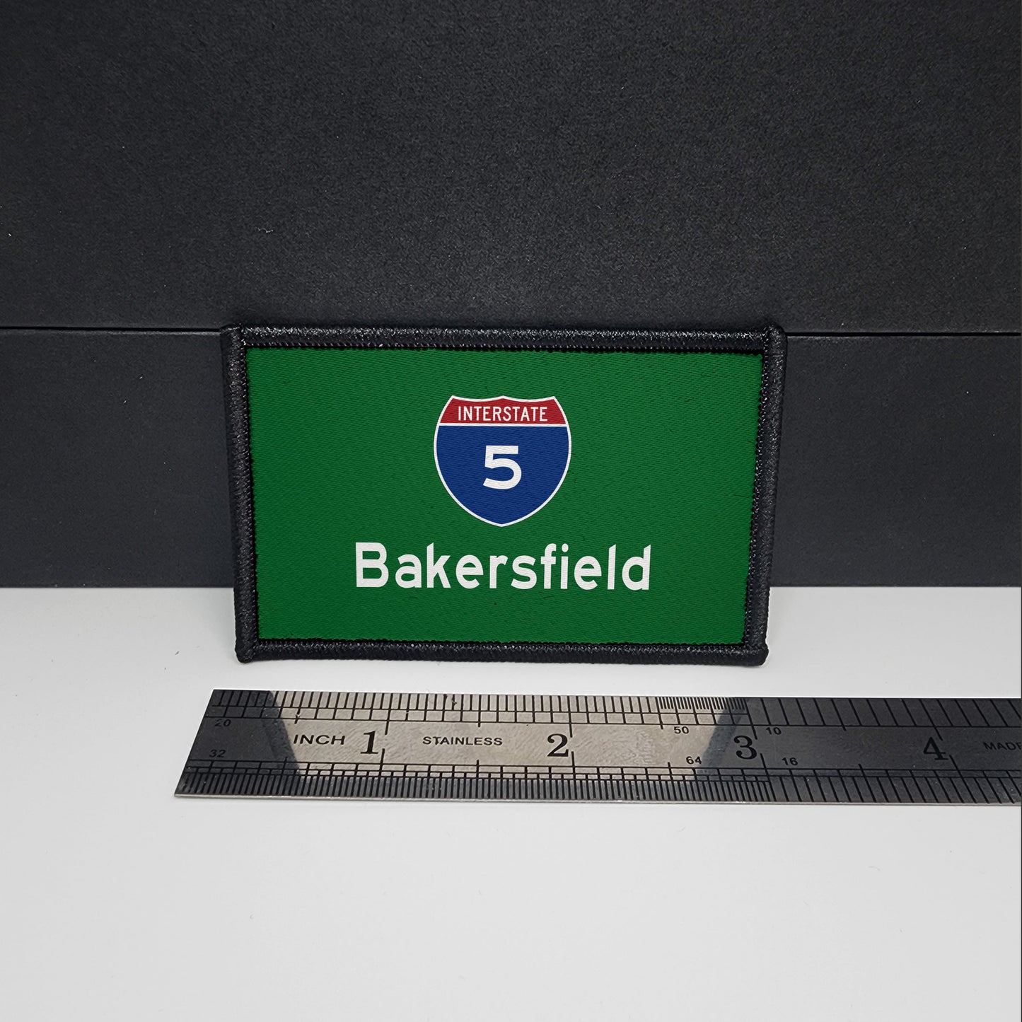 A rectangular patch with a green background featuring the 'Interstate 5 Bakersfield' text and a shield-shaped emblem, placed next to a ruler for scale.
CAPS LOCK ORIGINAL - patch - morale patch - 2x3 inch – hook and loop - iron-on - interchangeable patch - hat - bag -