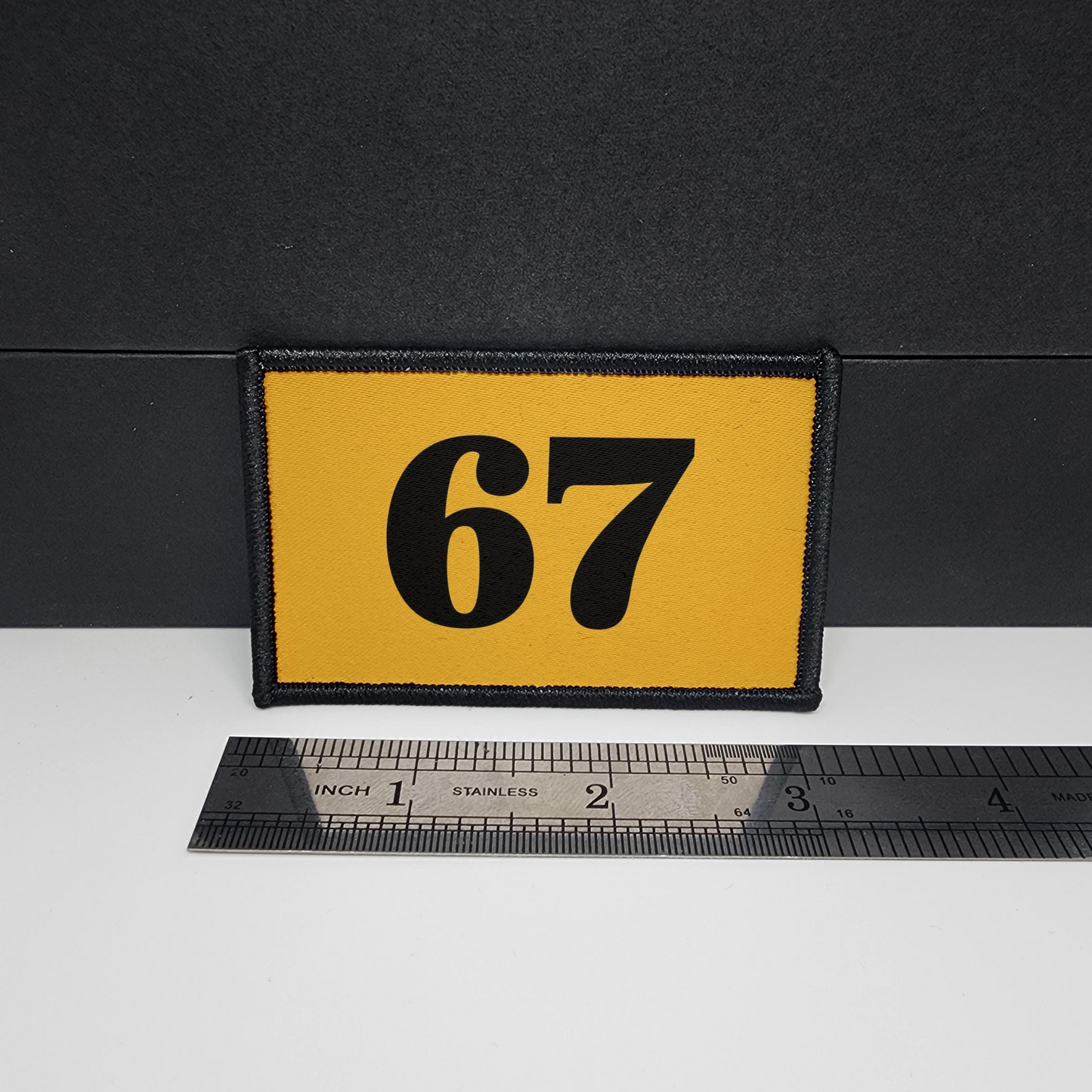 Yellow patch with the number 67 on a black background, measured against a ruler.

CAPS LOCK ORIGINAL - morale patch - 2x3 inch – hook and loop - iron-on - interchangeable patch - hat - bag