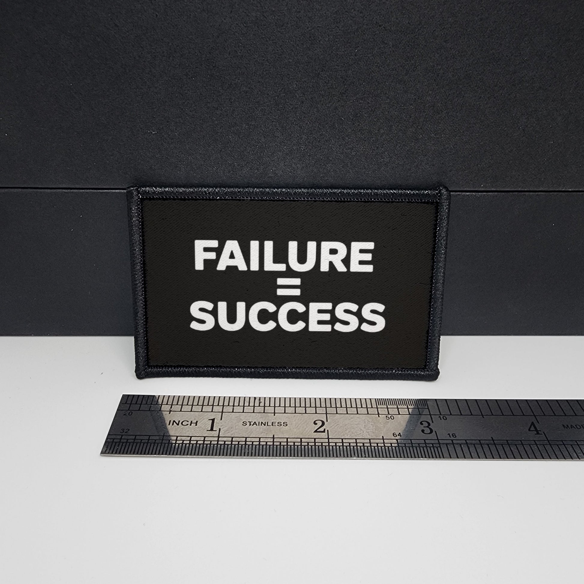 Black patch with 'FAILURE = SUCCESS' text on a white surface with a ruler for scale.

CAPS LOCK ORIGINAL - morale patch - 2x3 inch – hook and loop - iron-on - interchangeable patch - hat - bag - sports