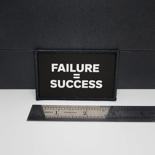 Black patch with 'FAILURE = SUCCESS' text on a white surface with a ruler for scale.

CAPS LOCK ORIGINAL - morale patch - 2x3 inch – hook and loop - iron-on - interchangeable patch - hat - bag - sports