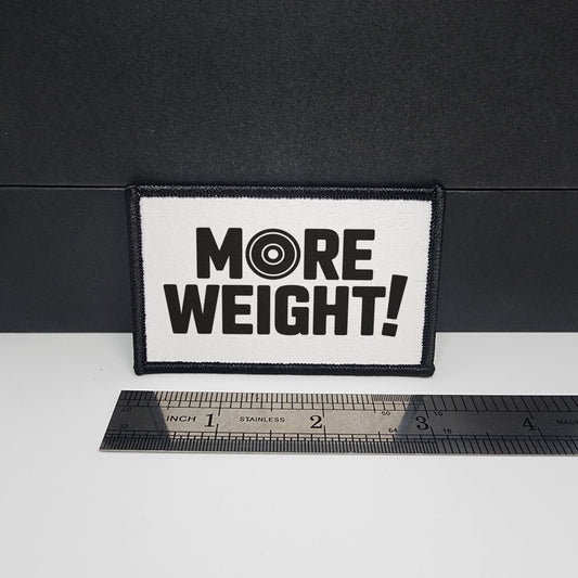 Patch with 'MORE WEIGHT!' text on a black background with a ruler for scale.