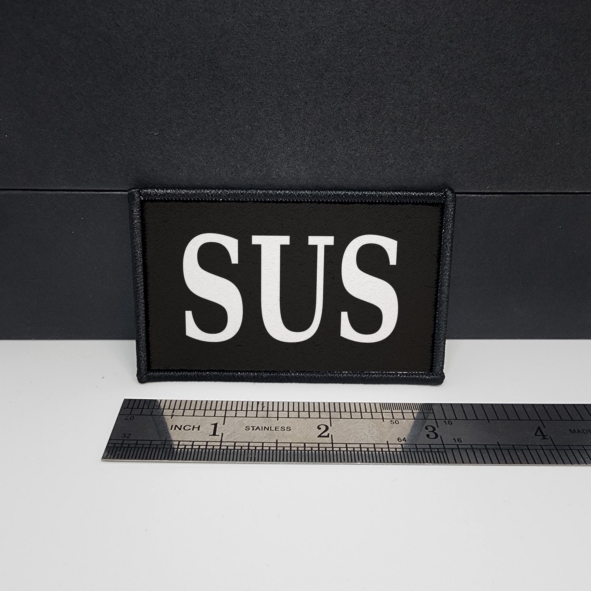 Black patch with 'SUS' text on a white surface with a ruler for scale.

CAPS LOCK ORIGINAL - morale patch - 2x3 inch – hook and loop - iron-on - interchangeable patch - hat - bag